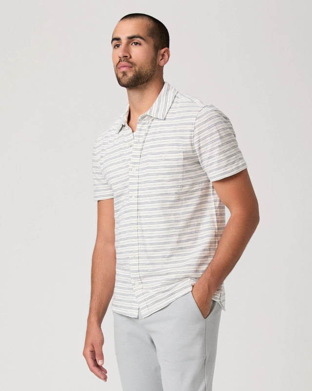 Man wearing a white striped shirt and light gray pants on a plain background
