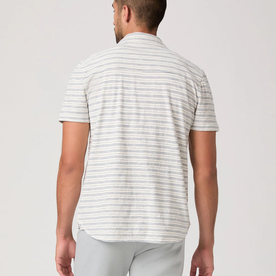 Man wearing a striped polo shirt and light gray pants on a white background