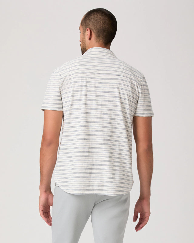Man wearing a striped polo shirt and light gray pants on a white background