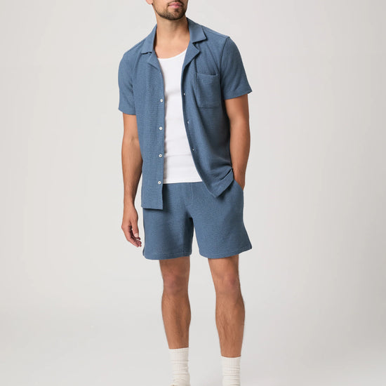 Person wearing blue Paige shorts and a matching shirt on a plain background