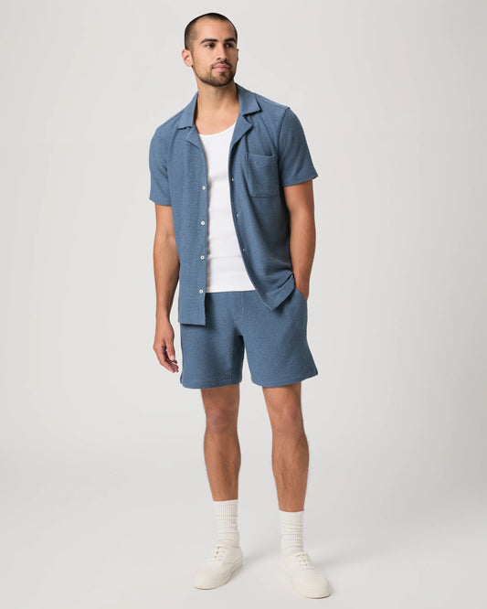 Person wearing blue Paige shorts and a matching shirt on a plain background