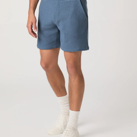 Person wearing blue Paige shorts and white shoes on a plain background