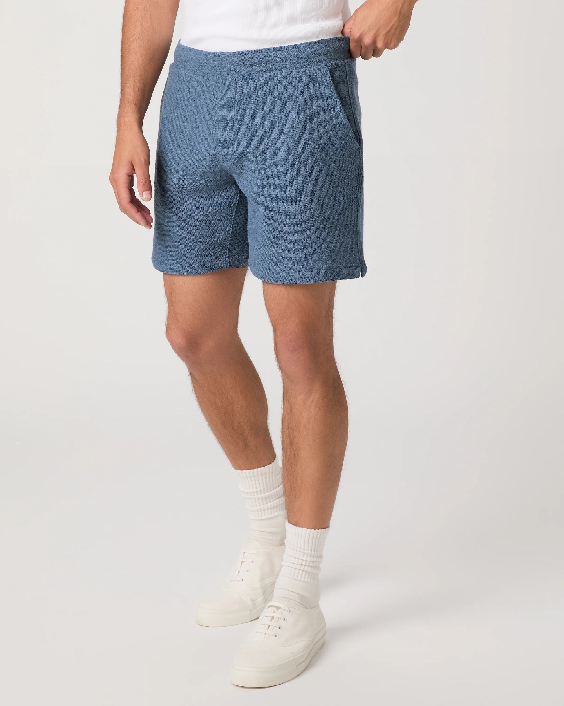 Person wearing blue Paige shorts and white shoes on a plain background