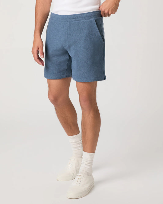 Person wearing blue Paige shorts and white shoes on a plain background