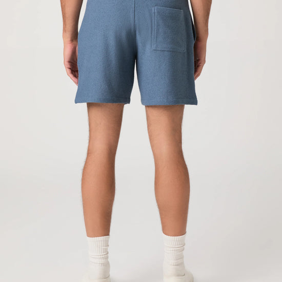Person wearing blue Paige shorts and white shoes on a plain background rear view