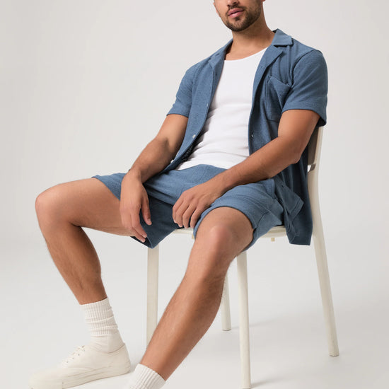 Person wearing blue Paige shorts and matching shirt sat on a chair with a plain background