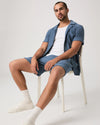 Person wearing blue Paige shorts and matching shirt sat on a chair with a plain background