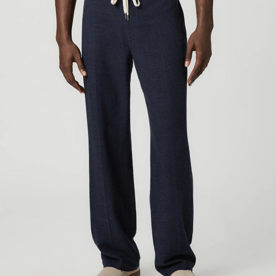 Navy blue pants with a white drawstring by Paige worn by a man on a light gray background