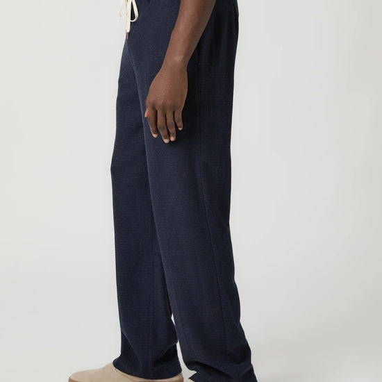 Navy blue pants with a white drawstring by Paige worn by a man on a light gray background side view
