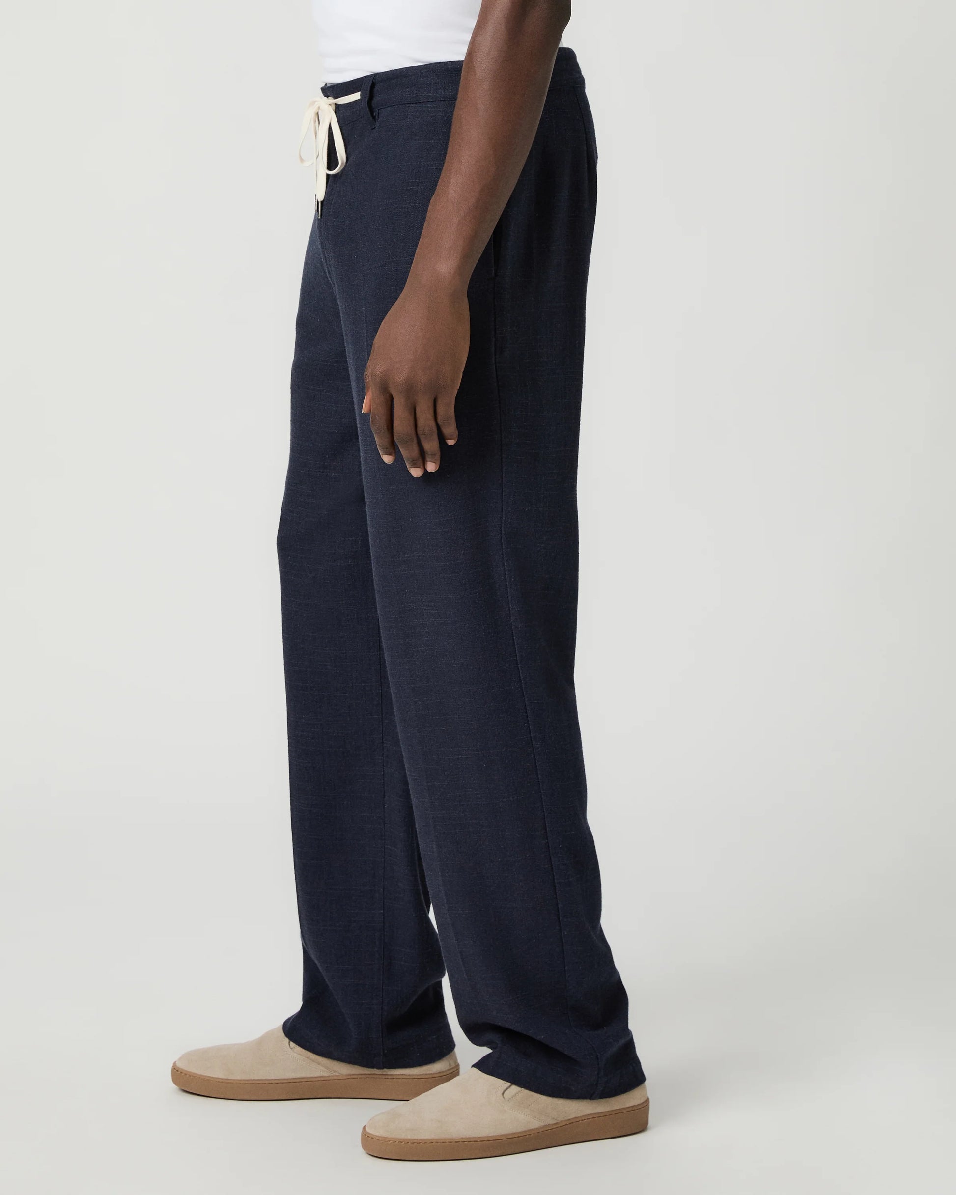 Navy blue pants with a white drawstring by Paige worn by a man on a light gray background side view