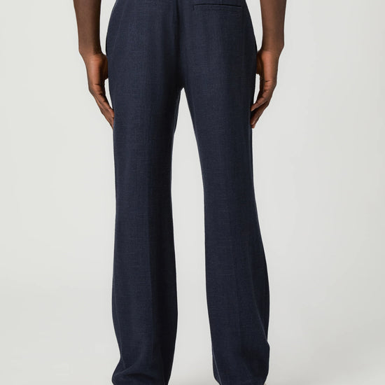Navy blue pants with a white drawstring by Paige worn by a man on a light gray background rear view