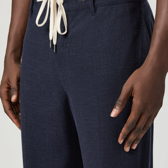 Navy blue pants with a white drawstring by Paige worn by a man on a light gray background close up