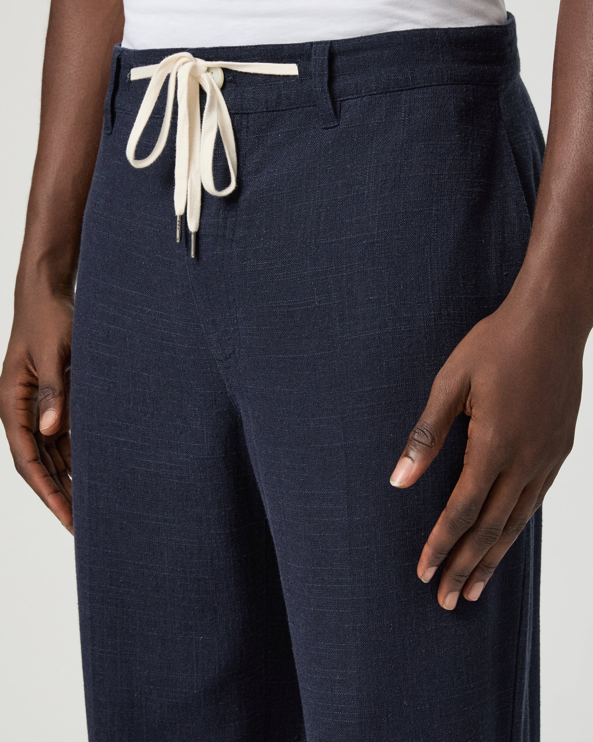 Navy blue pants with a white drawstring by Paige worn by a man on a light gray background close up