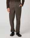 A person wearing dark brown straight-leg trousers, a dark brown long-sleeve top, and black shoes, shown from the waist down against a light gray studio background.
