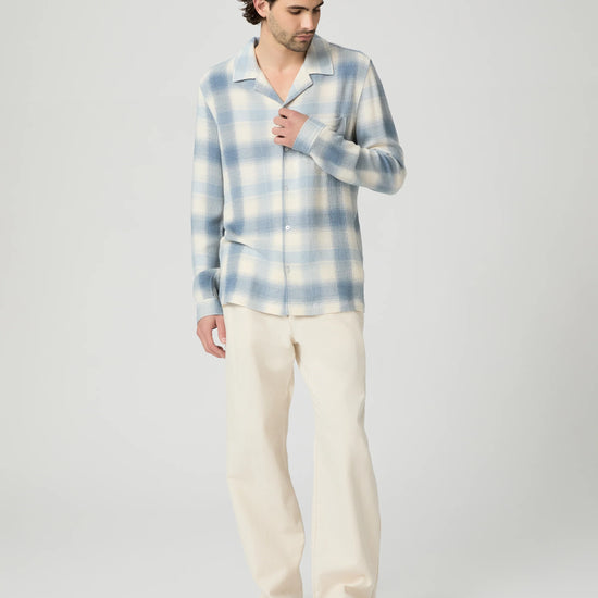 Man wearing a blue and white checkered shirt and beige pants on a light gray background from Paige