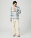 Man wearing a blue and white checkered shirt and beige pants on a light gray background from Paige