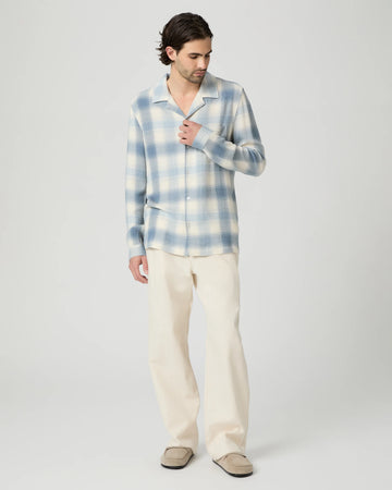 Man wearing a blue and white checkered shirt and beige pants on a light gray background from Paige