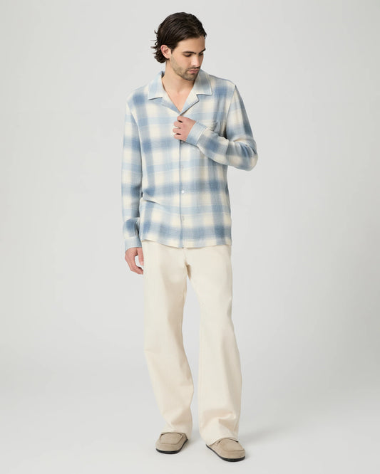 Man wearing a blue and white checkered shirt and beige pants on a light gray background from Paige