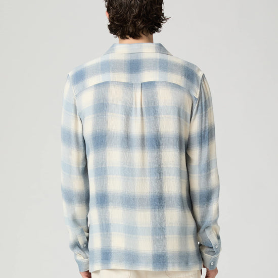 Person wearing a blue and white checkered shirt on a gray background from Paige