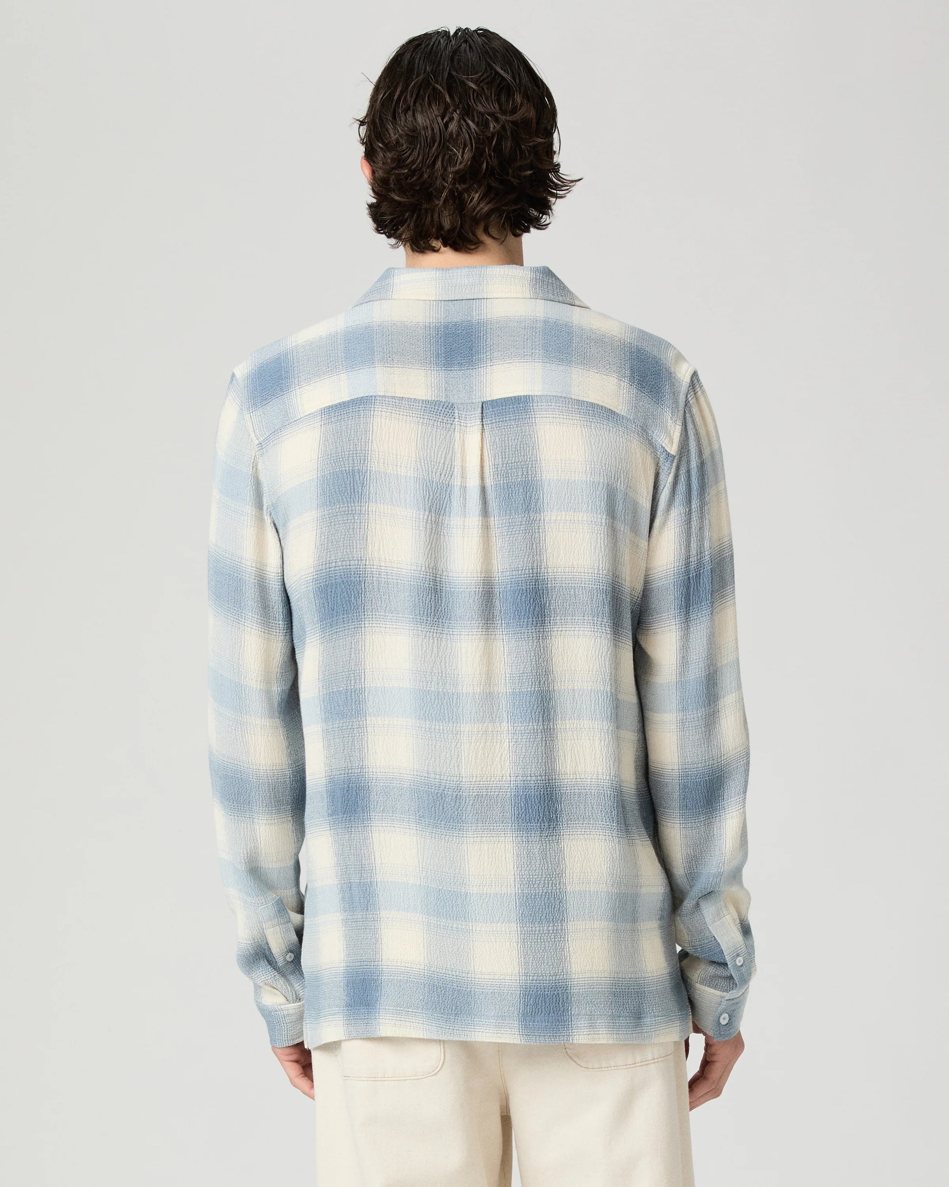 Person wearing a blue and white checkered shirt on a gray background from Paige