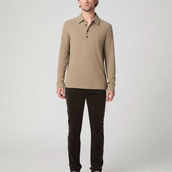 A man modeling a beige long-sleeve polo shirt with dark brown pants and beige shoes, standing against a light gray studio background.