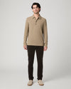 A man modeling a beige long-sleeve polo shirt with dark brown pants and beige shoes, standing against a light gray studio background.