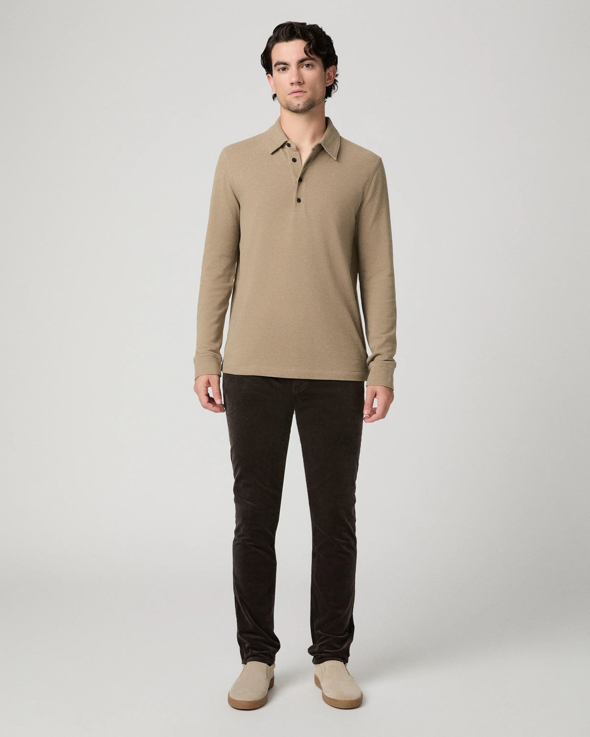 A man modeling a beige long-sleeve polo shirt with dark brown pants and beige shoes, standing against a light gray studio background.