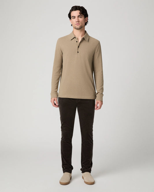 A man modeling a beige long-sleeve polo shirt with dark brown pants and beige shoes, standing against a light gray studio background.