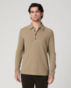 A man wearing a beige long-sleeve polo shirt with a three-button placket, paired with dark pants, standing against a light gray studio background.