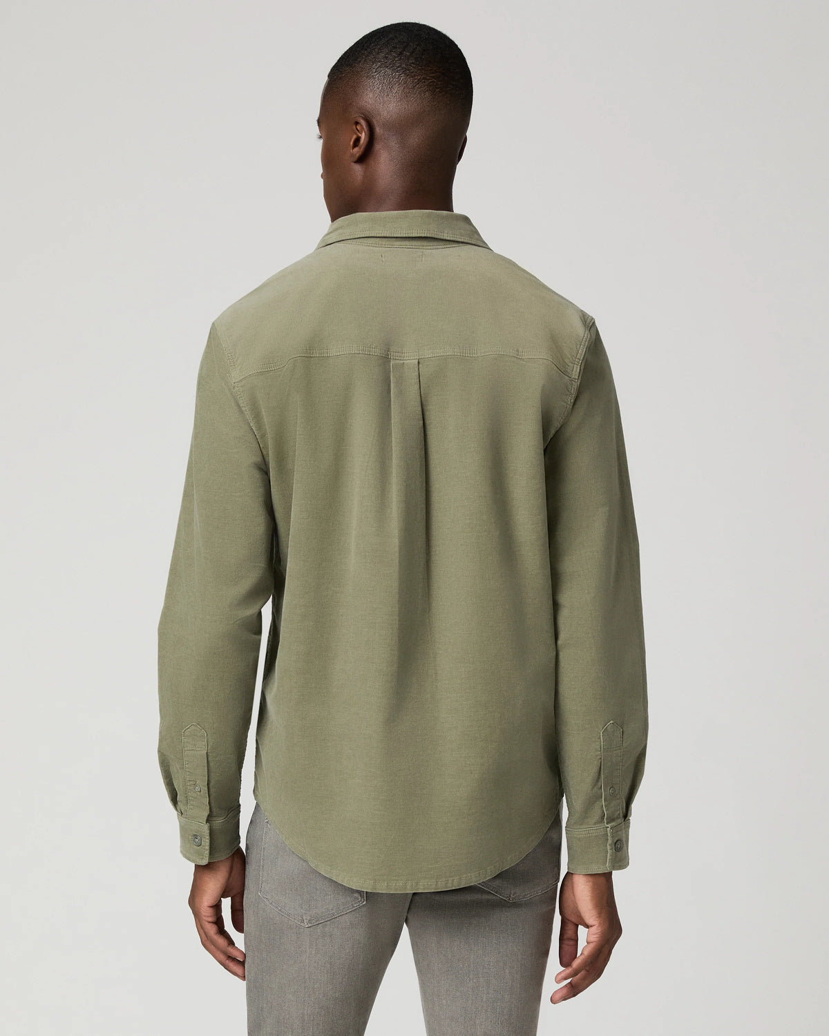 A man viewed from the back wearing a muted sage green long-sleeve button-up shirt and gray trousers, photographed against a plain light gray studio background.