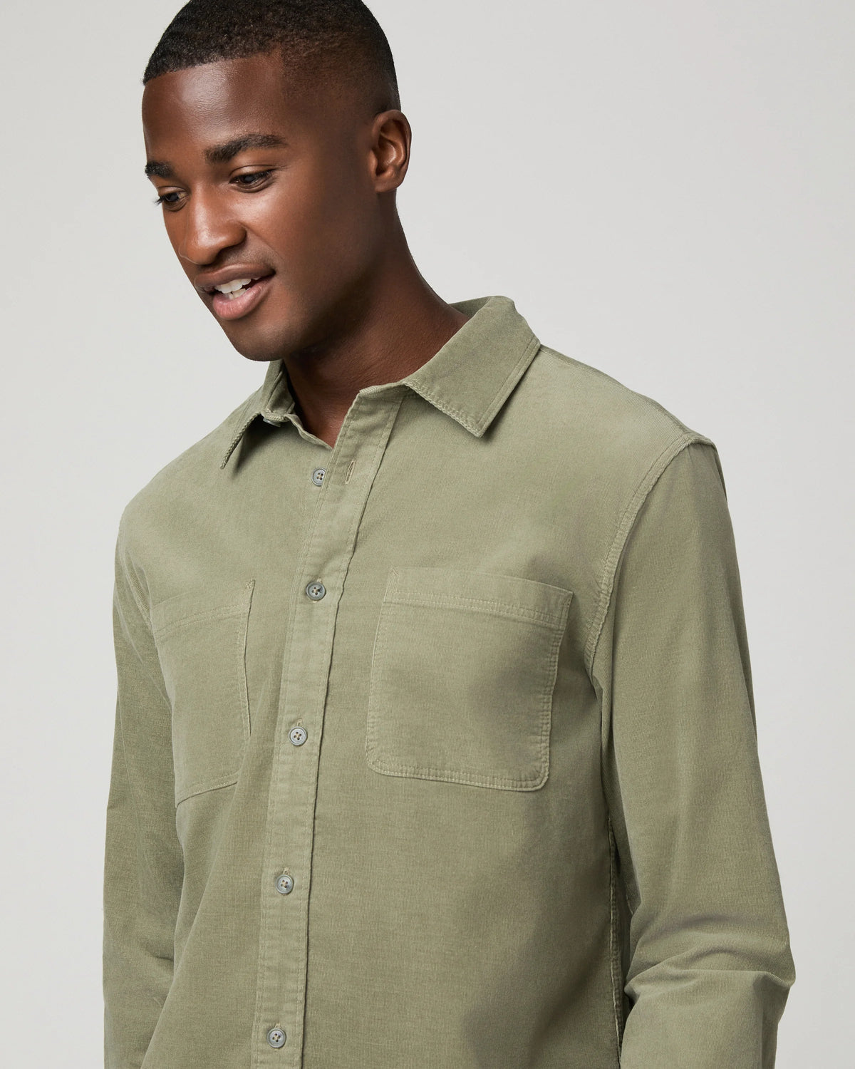 A man wearing a light olive green long-sleeve button-up shirt with two chest pockets, photographed against a neutral light gray background.