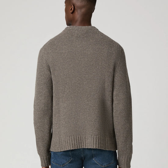 A man viewed from the back wearing a taupe brown ribbed knit sweater and blue jeans, set against a plain light gray studio background.