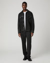 A man modeling a black denim jacket and matching black jeans over a white t-shirt, standing against a light gray studio background.
