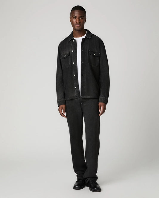 A man modeling a black denim jacket and matching black jeans over a white t-shirt, standing against a light gray studio background.