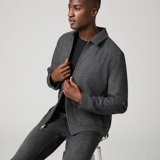 Man sat down wearing grey zip jacket and black jeans 