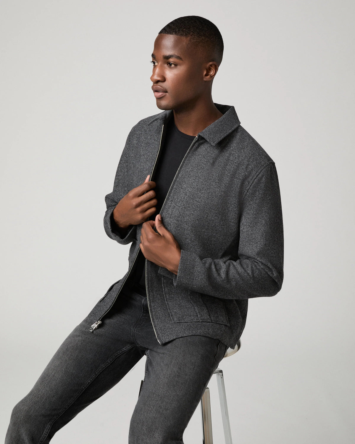 Man sat down wearing grey zip jacket and black jeans 