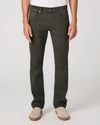 A person wearing dark olive green slim-fit jeans with a white t-shirt and beige slip-on shoes, shown from the waist down on a light gray studio background.