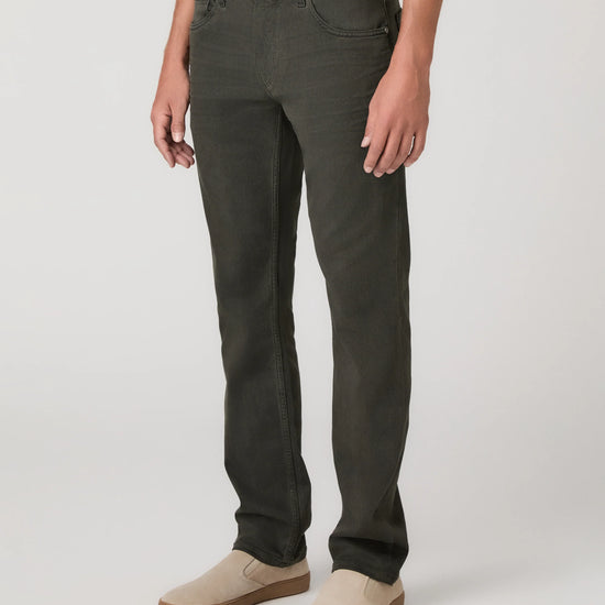 A person wearing dark olive green slim-fit jeans with beige slip-on shoes, shown from the waist down against a light gray studio background.