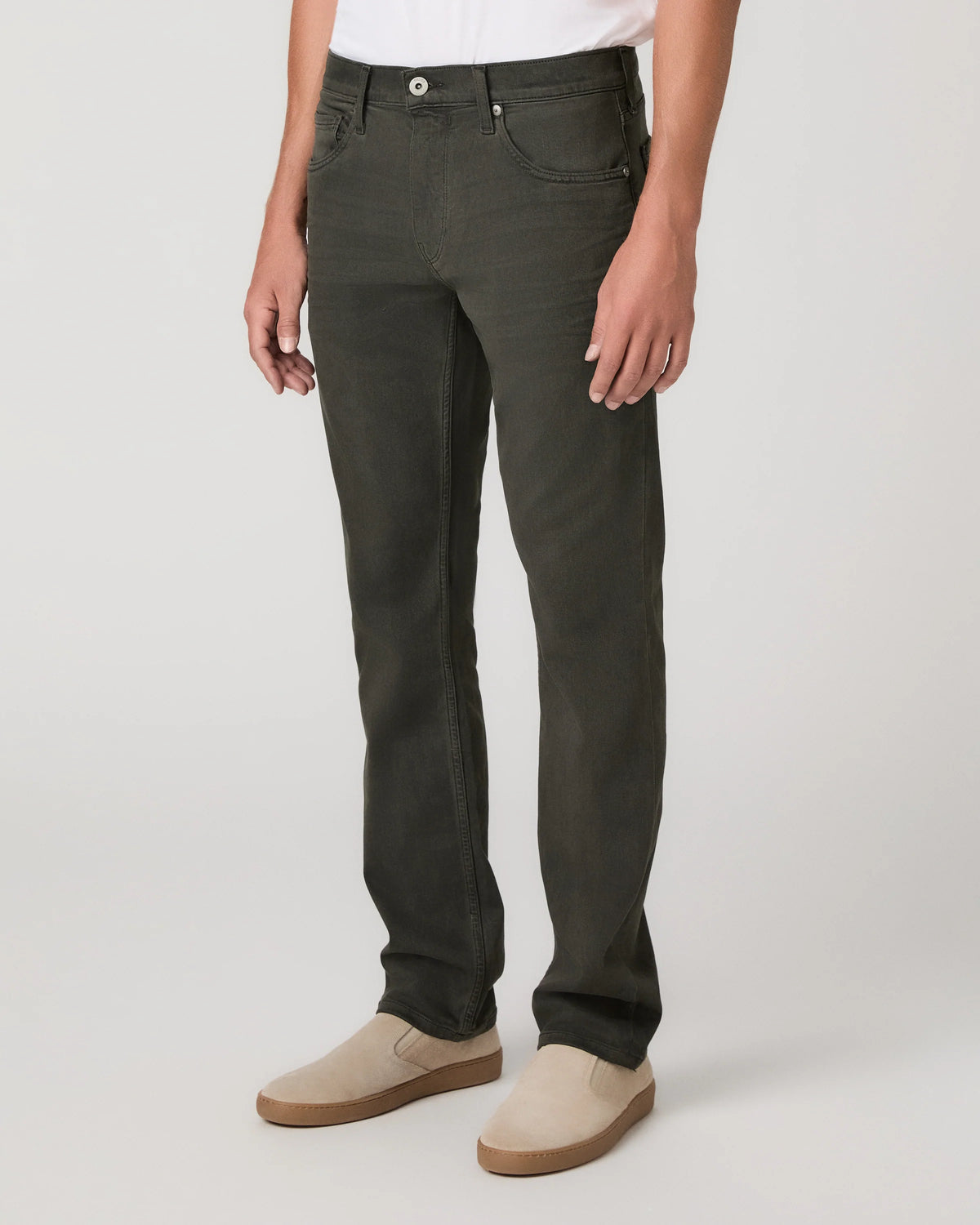 A person wearing dark olive green slim-fit jeans with beige slip-on shoes, shown from the waist down against a light gray studio background.
