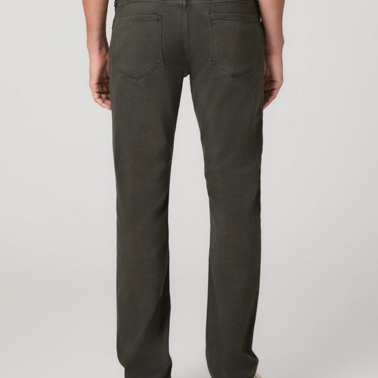 Rear view of a person wearing dark olive green straight-leg jeans with a white shirt and tan shoes, photographed against a light gray studio background.