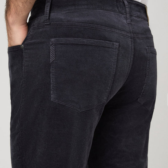 Close-up back view of a person wearing dark charcoal corduroy trousers, showing the back pocket detail and waistband.