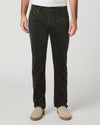 A person wearing dark charcoal corduroy trousers, styled with a white t-shirt and beige slip-on shoes, photographed against a neutral light gray studio background.