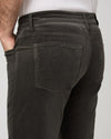 Close-up back view of a person wearing dark charcoal corduroy pants, showing the back pockets and waistband against a light gray studio background.