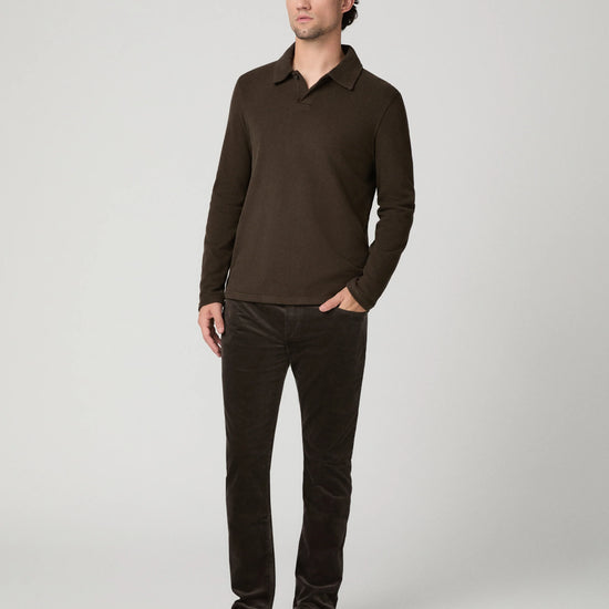 A man modeling a dark brown long-sleeve polo shirt and matching dark brown corduroy trousers against a light gray studio background.