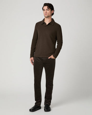 A man modeling a dark brown long-sleeve polo shirt and matching dark brown corduroy trousers against a light gray studio background.