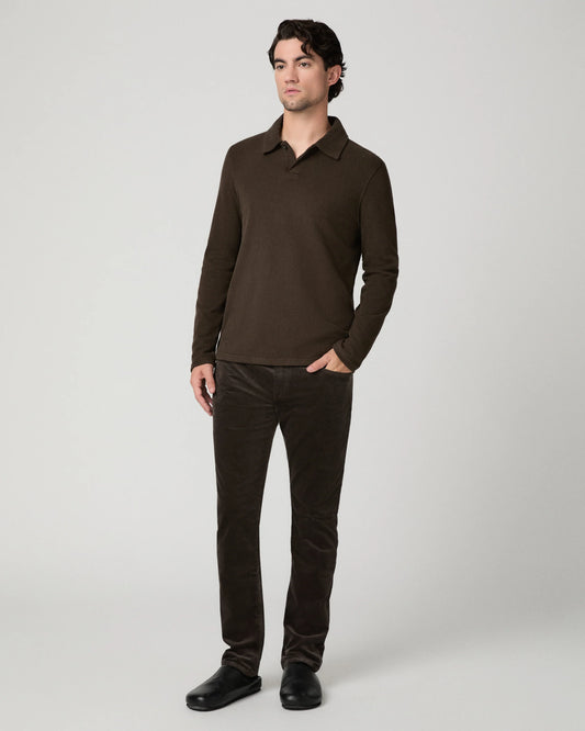A man modeling a dark brown long-sleeve polo shirt and matching dark brown corduroy trousers against a light gray studio background.