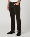 A person wearing dark brown corduroy trousers, styled with a white shirt and black shoes, shown from the waist down against a light gray studio background.