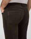 Close-up back view of a person wearing dark brown corduroy trousers, showing the back pocket and waistband against a light gray background.