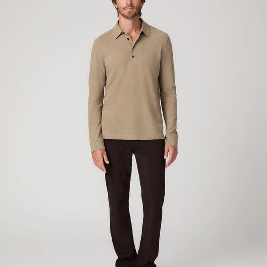 A man modeling a beige long-sleeve knit polo shirt with dark brown trousers and beige slip-on shoes, standing against a light gray studio background.