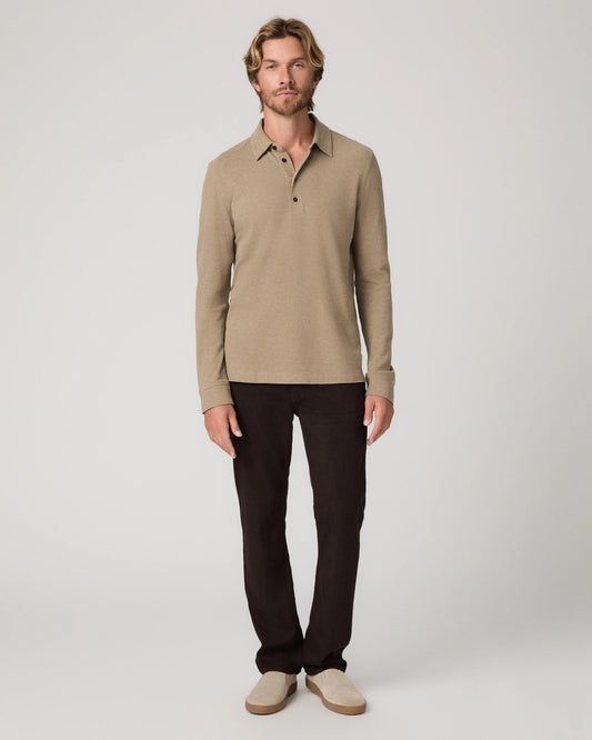 A man modeling a beige long-sleeve knit polo shirt with dark brown trousers and beige slip-on shoes, standing against a light gray studio background.